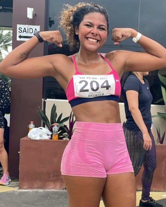 Ju sorrindo e mostrando os braços com o número de inscrição no peito, no dia do teste físico